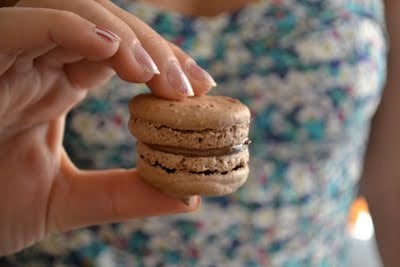 A hand holding a chocolate macaron with nutella filling.