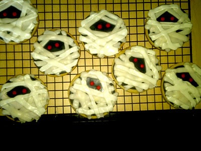 Sugar cookies decorated like mummies on a cooling rack.