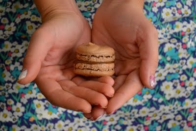 Two hands holding a chocolate macaron with nutella filling.