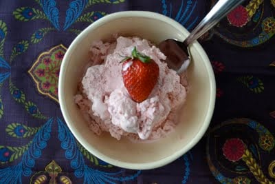 A bowl of strawberry ice cream with a spoon and fresh strawberry on top. 