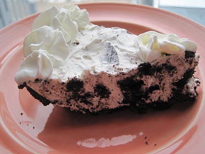 A slice of oreo pie topped with whipped cream on a pink plate.