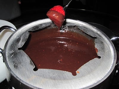 A fondue pot with chocolate fondue and a skewer of strawberry dipped in the chocolate.